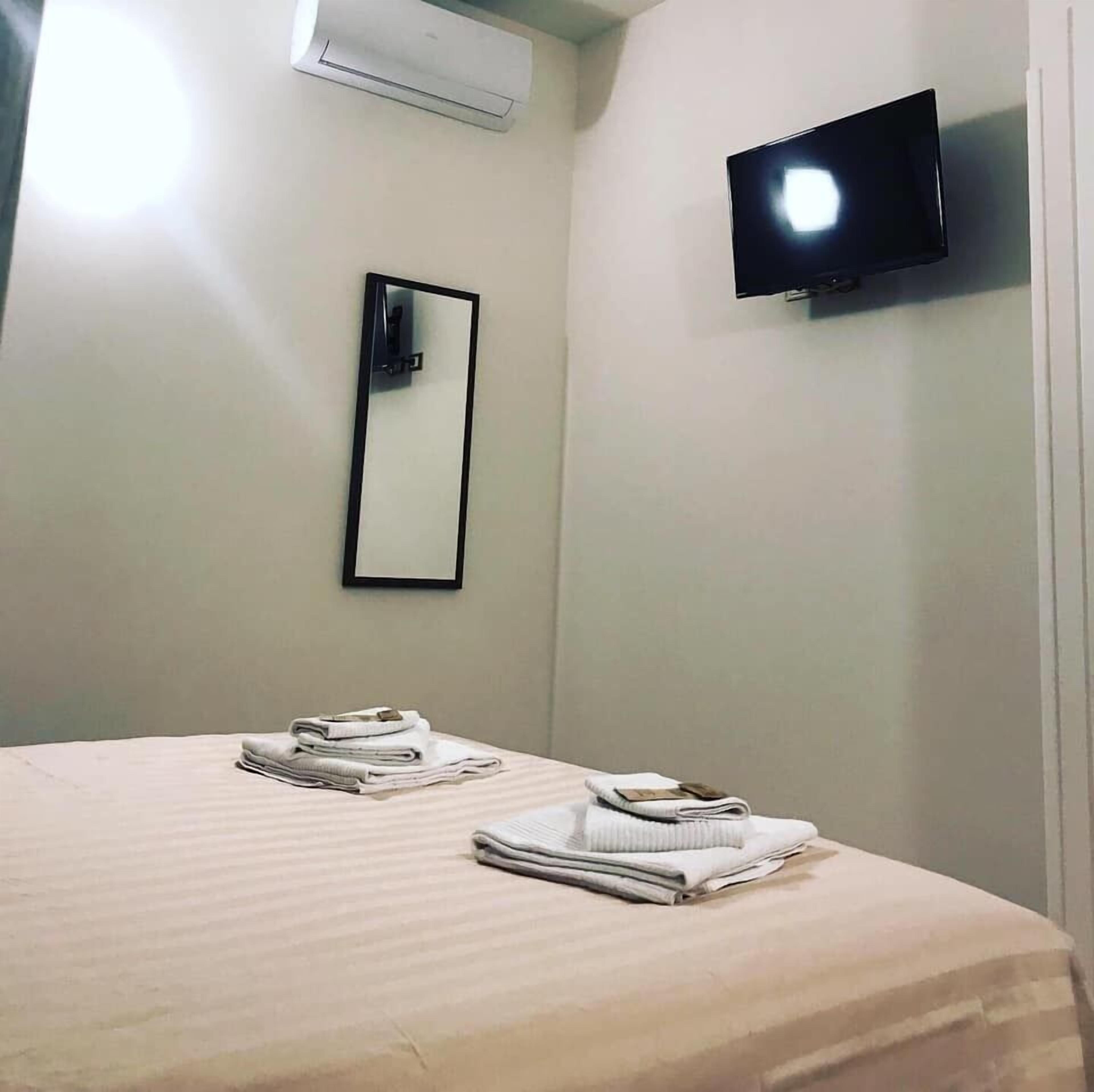 A hotel room with a bed, a flat-screen TV mounted on the wall, and a mirror.