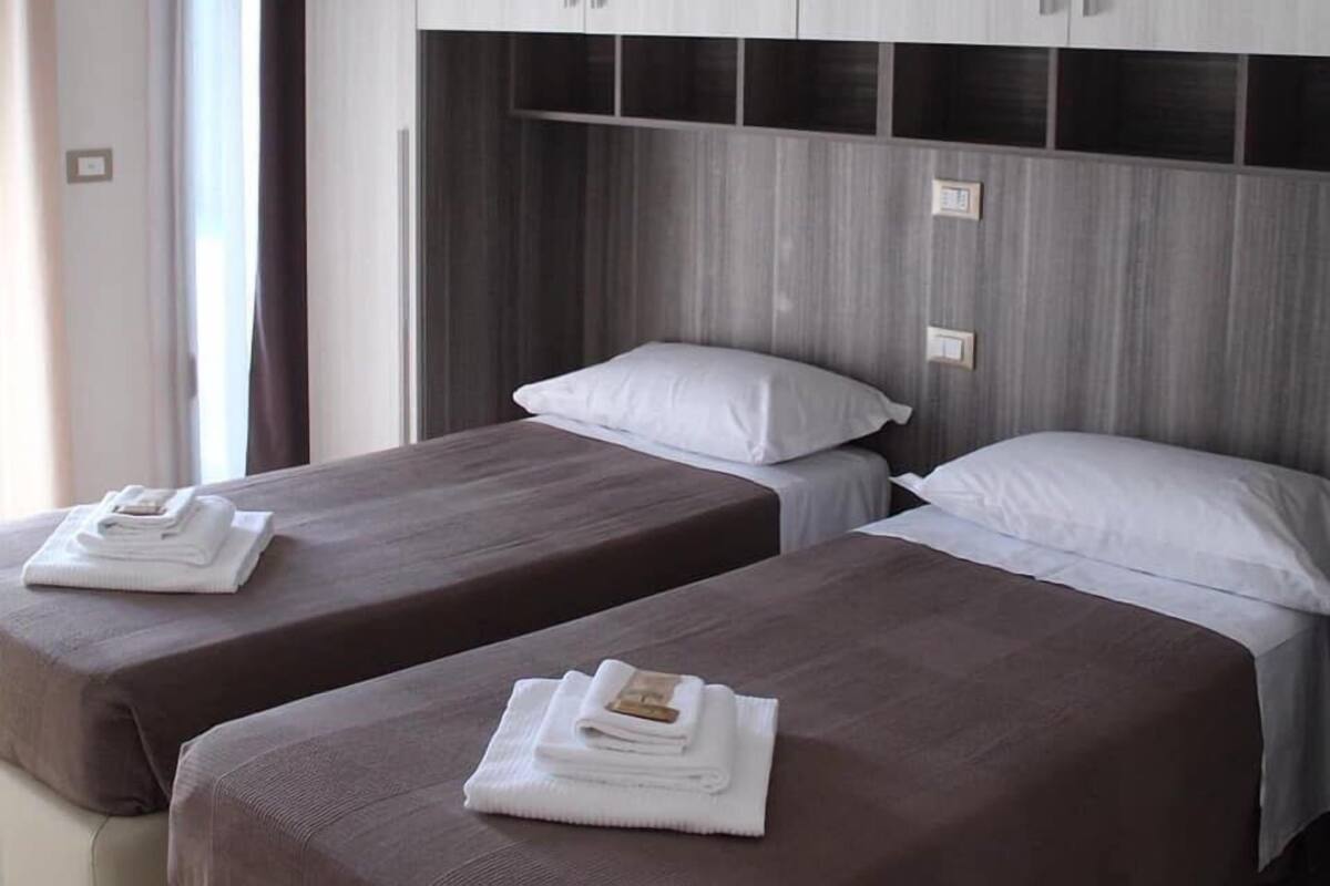 A hotel room with two single beds, each with a neatly folded towel and a pillow.