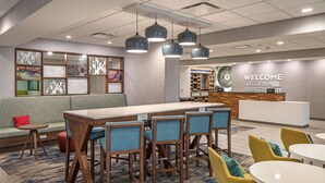 A modern hotel lobby with a reception desk, seating area, and a bar. - Hampton Inn Hastings (Hastings)