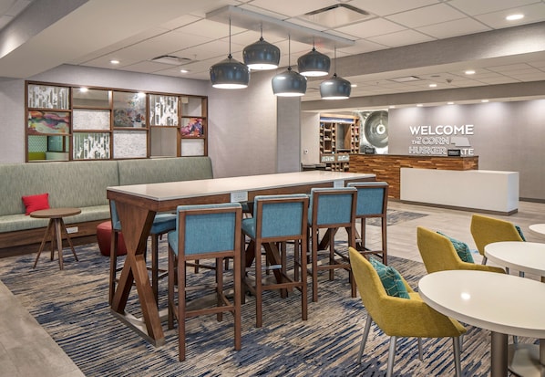 A modern hotel lobby with a reception desk, seating area, and a bar.