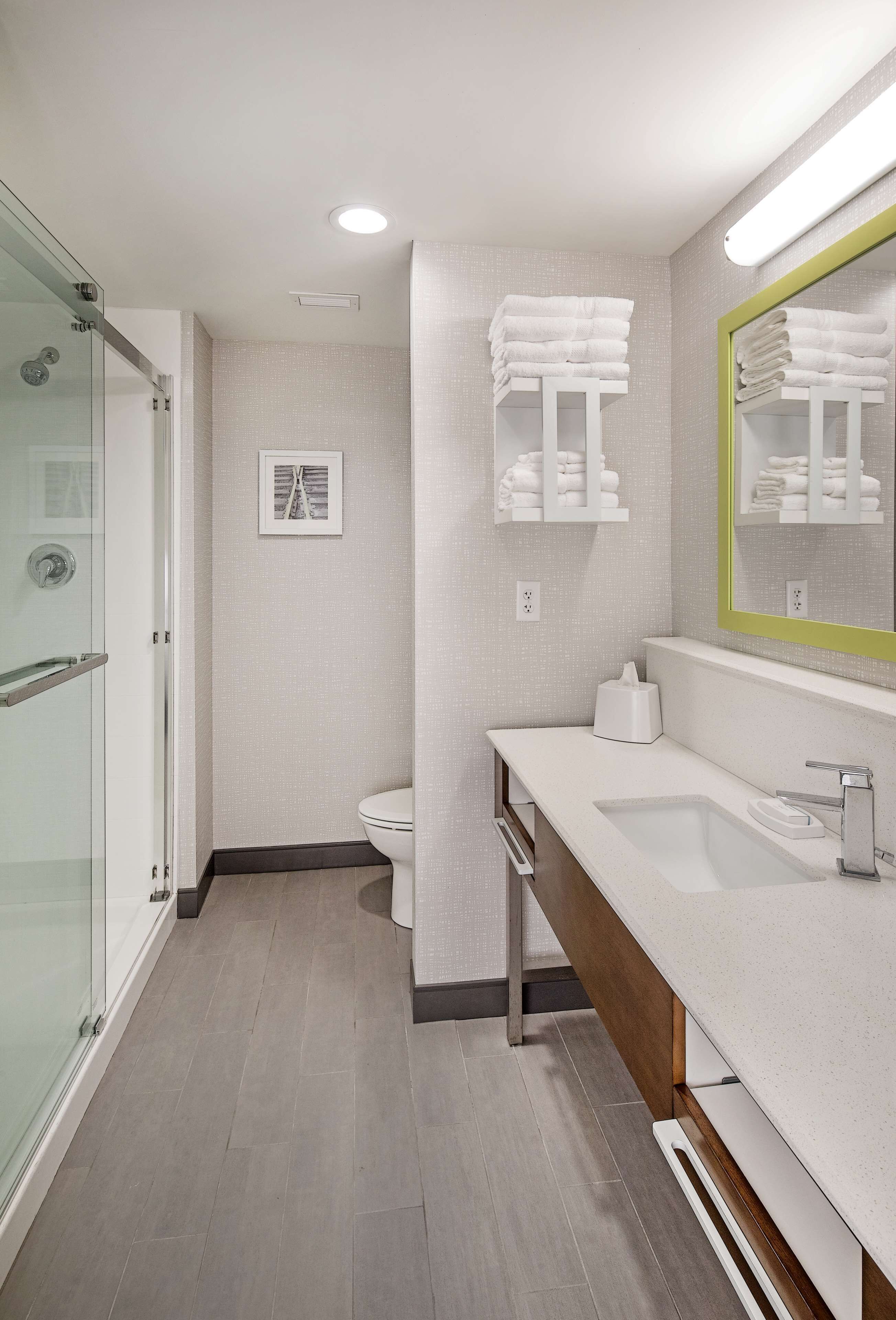 A modern bathroom with a glass shower enclosure, a white sink with a wooden vanity, and a mirror with a green frame.