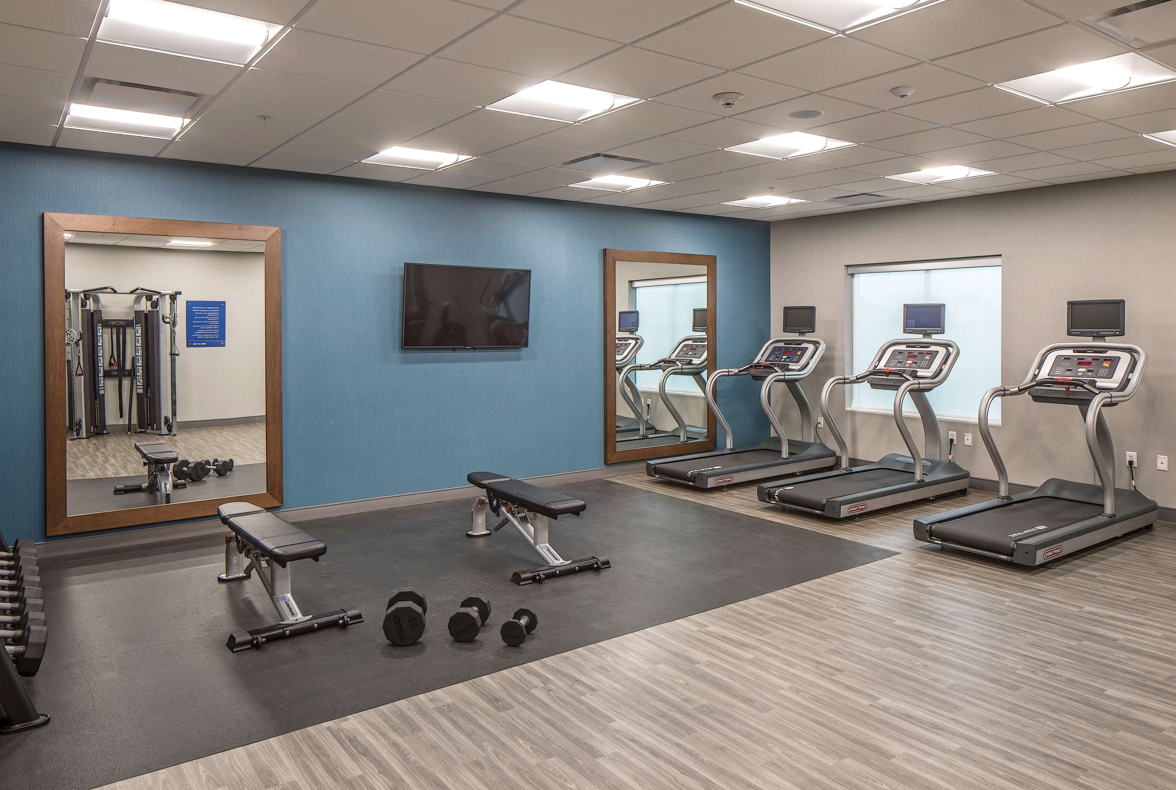 Een fitnessruimte met loopbanden, gewichten, een bank en een spiegel.