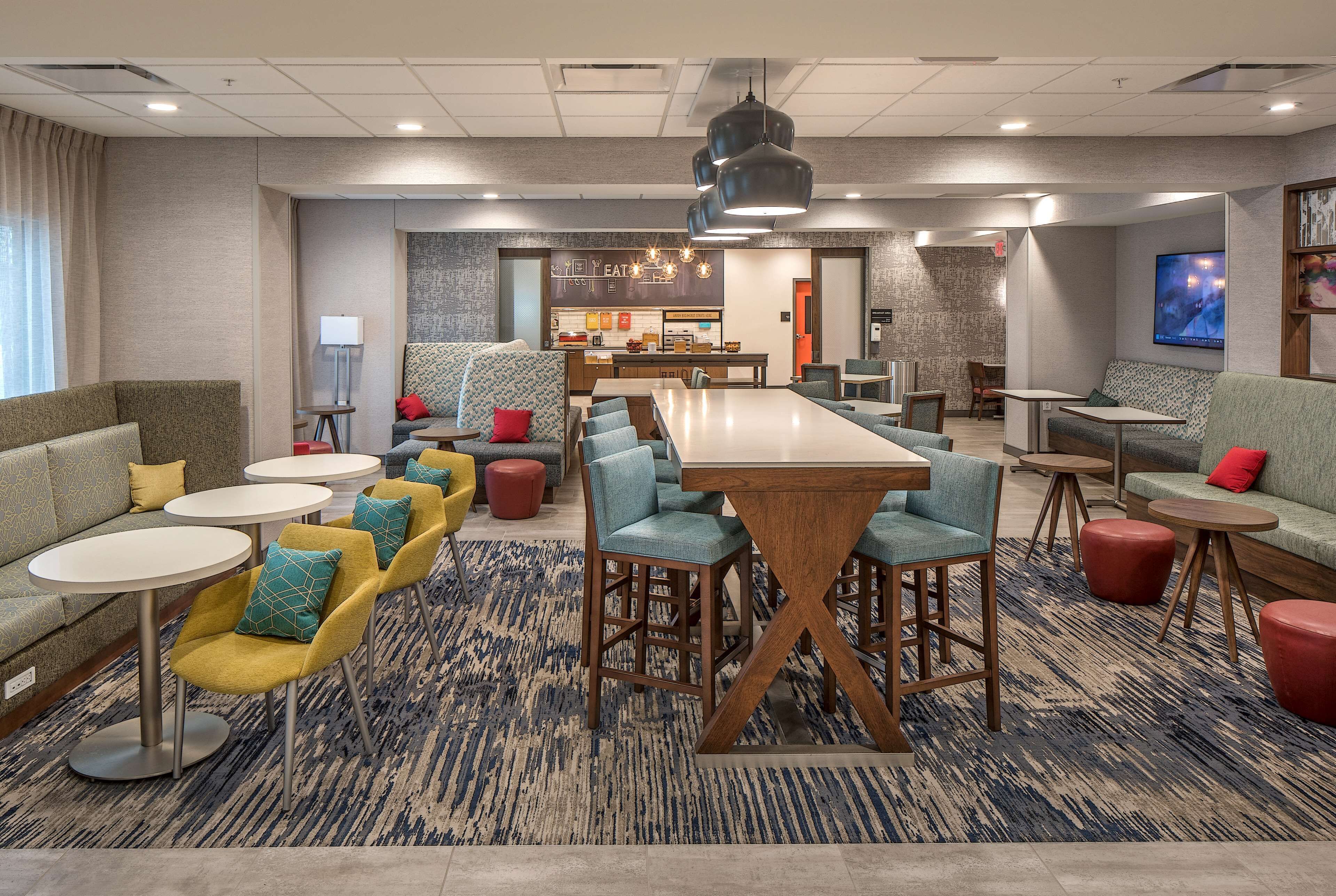 A hotel lobby with a long communal table, several sofas, and round tables.