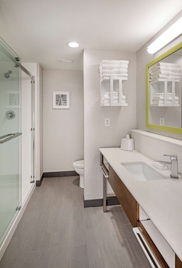 A modern bathroom with a glass shower enclosure, a white sink with a wooden vanity, and a mirror with a green frame.