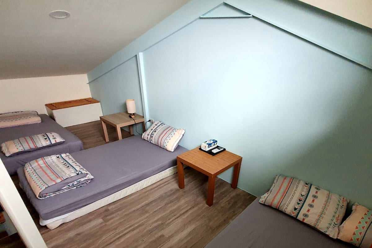 A compact room with two beds, a small table, and a bench.