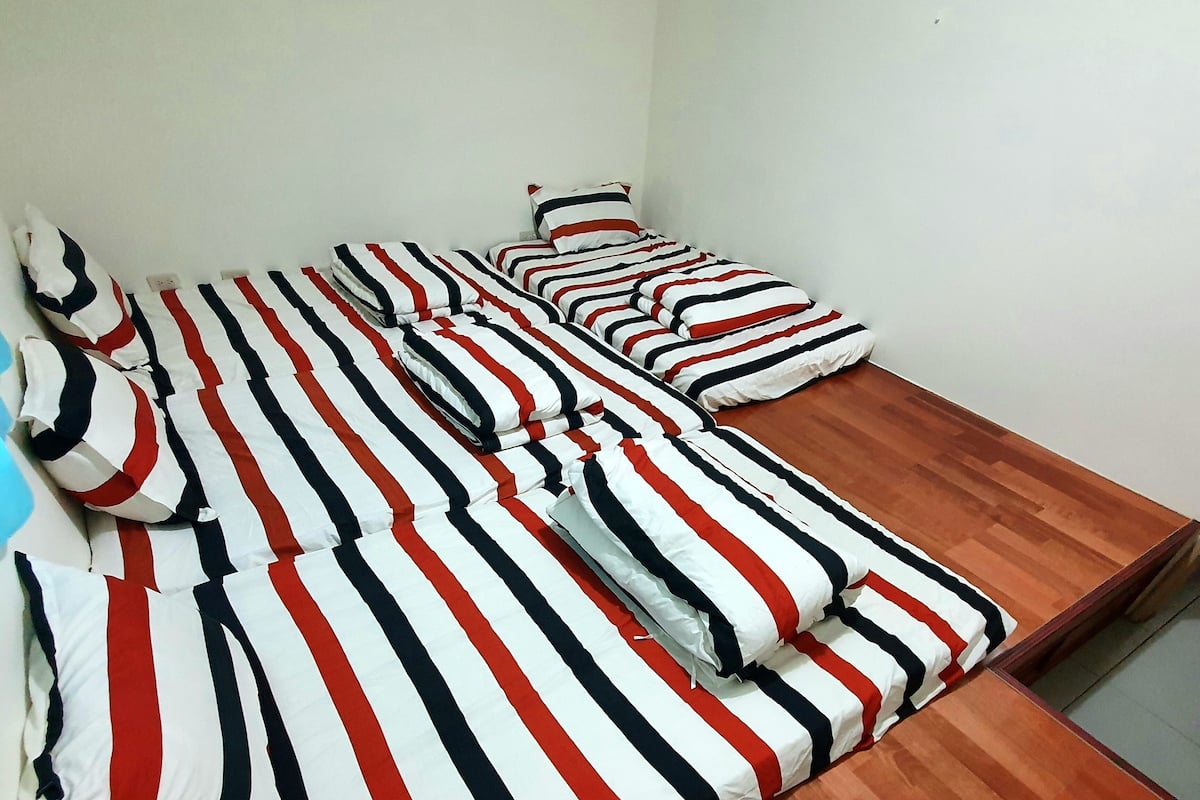 A room with a long wooden bed with striped bedding and pillows.