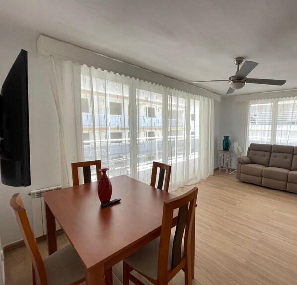 A living room with a dining table, chairs, a sofa, a TV, and a ceiling fan.