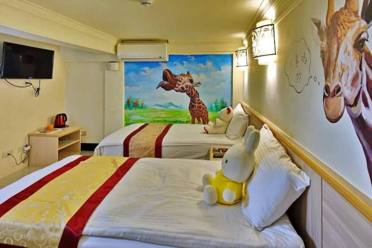 A hotel room with two beds, a painting of a giraffe, a stuffed toy, and a television on the wall.