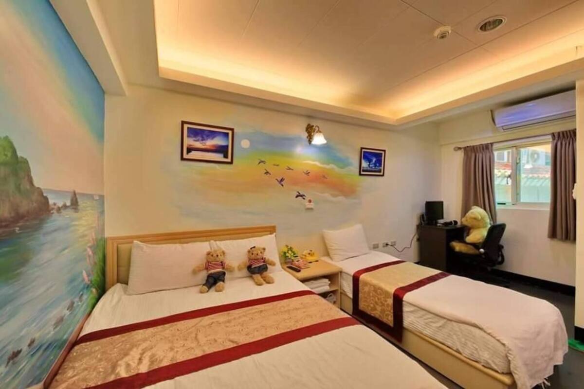 A hotel room with two beds, a desk, a chair, and a large mural on the wall.