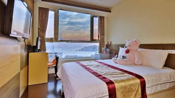 A hotel room with a bed, a desk, a television, and a large window with a view of the sea. - Shangrila (Dongyin Town)