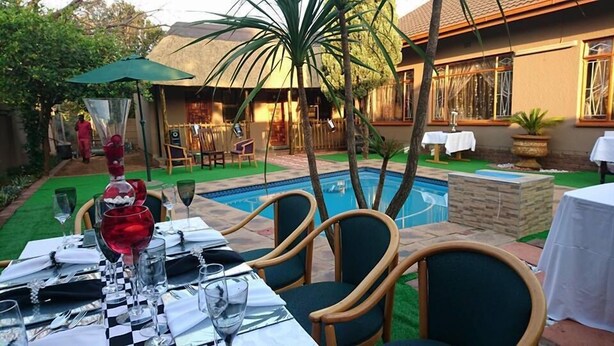 Un comedor con piscina, asientos exteriores y una construcción con techo de paja.