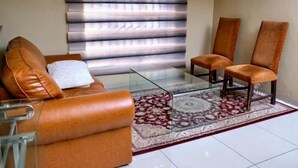 Uma sala de estar com sofá, duas poltronas, mesa de centro de vidro e tapete estampado.