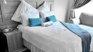 Una cama bien hecha con almohadas blancas y azules, una toalla enrollada y una manta azul.