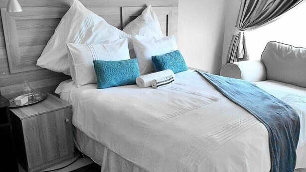 Cama bem arrumada com almofadas brancas e azuis, uma toalha enrolada e um cobertor azul.