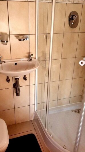 Un baño con lavamanos, inodoro y cabina de ducha con mampara de vidrio.