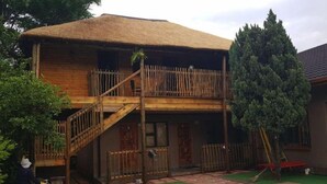 Una casa de dos pisos con techo de paja, un balcón de madera y una piscina.