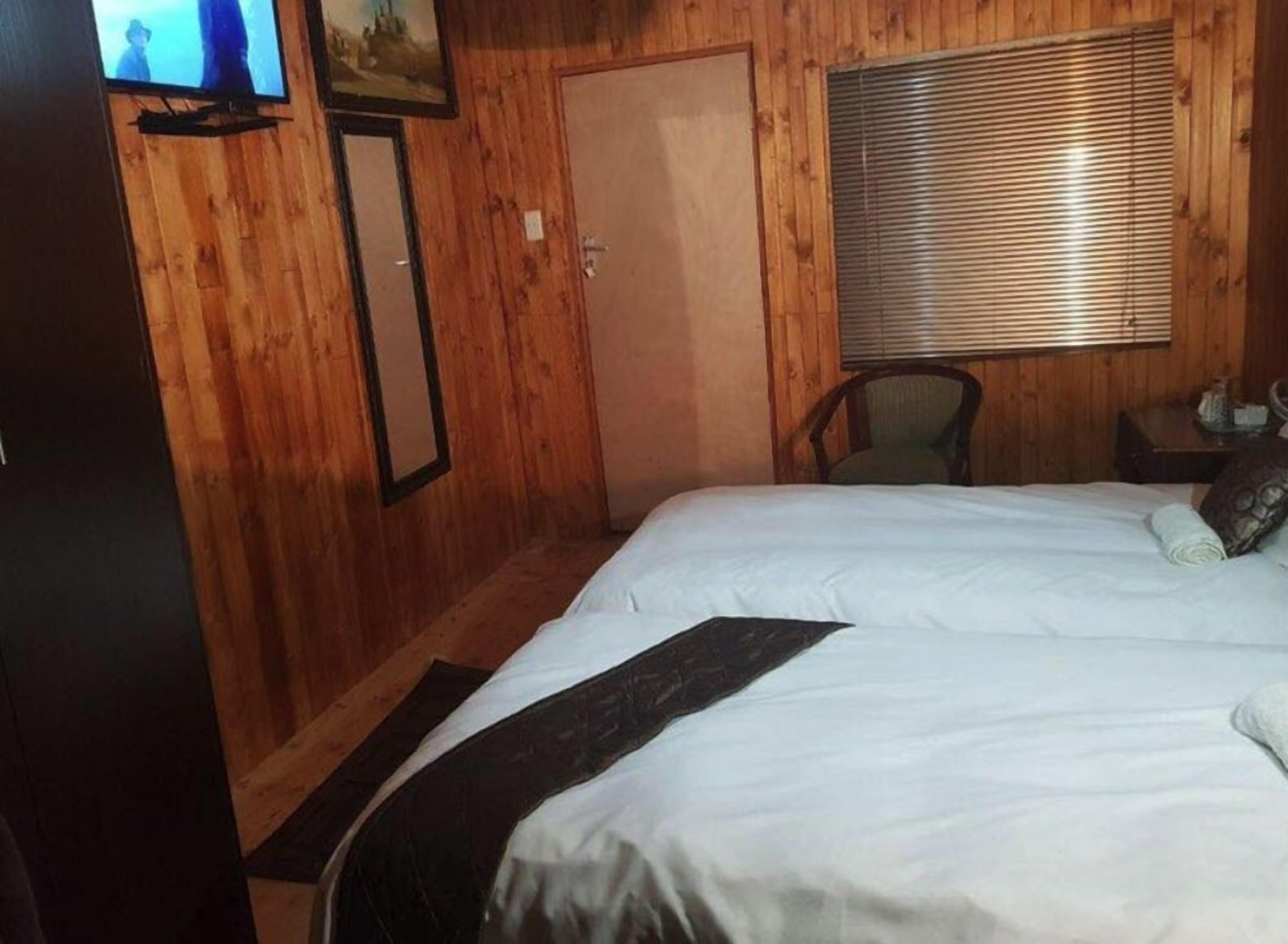 Una stanza con rivestimenti in legno, un letto, una sedia, una televisione e una finestra con persiane.