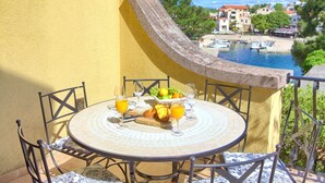 A balcony with a table set for breakfast, overlooking a marina and buildings. - Summer House Magdalena (Malinska-Dubasnica)