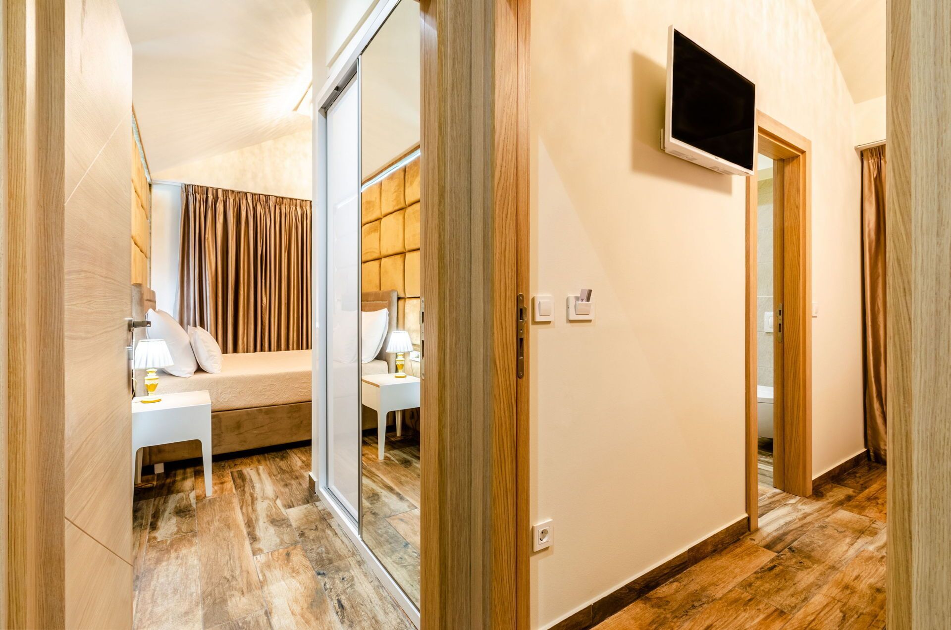 A hotel room with a bed, bedside table, lamp, and a TV mounted on the wall.