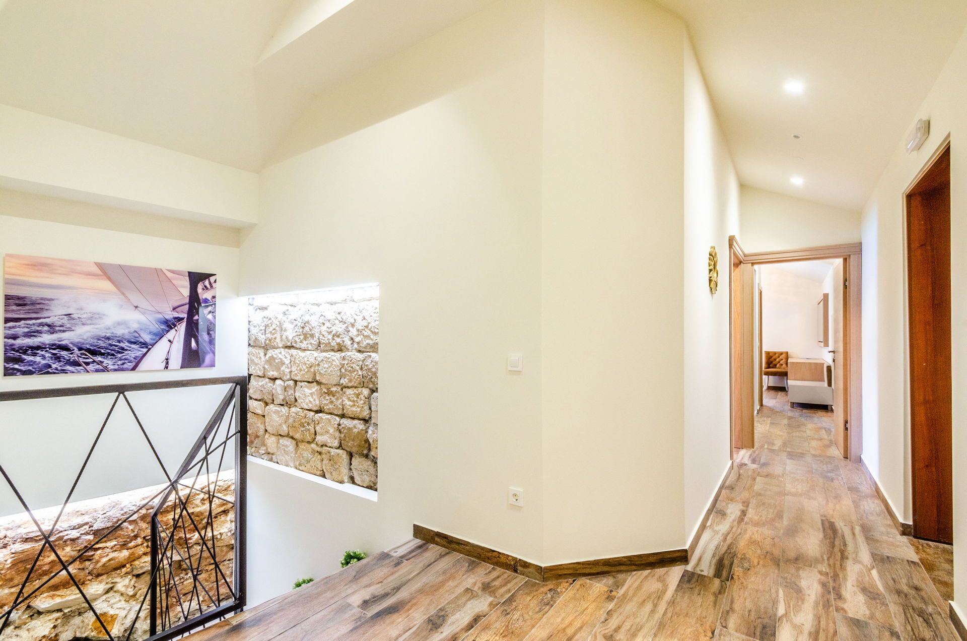A modern hallway with a stone accent wall, a wooden floor, and a view into a bedroom.