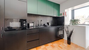 A modern kitchen with dark cabinetry, a tiled backsplash, and a window with a view of buildings. - Nomad's Family - 2BDR Spacious Apartment Gaia (Vila Nova de Gaia)