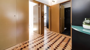 A hallway with wooden doors, a checkered wooden floor, and a black wall with a white object on it. - Nomad's Family - 2BDR Spacious Apartment Gaia (Vila Nova de Gaia)