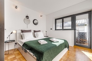 Une chambre à coucher avec un lit, des tables de chevet, un miroir et une fenêtre avec des stores.