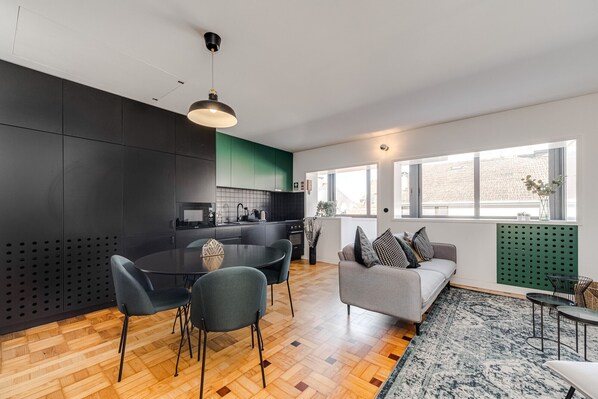 Une cuisine moderne avec des meubles de couleur sombre, une table à manger avec des chaises et un canapé avec des coussins.