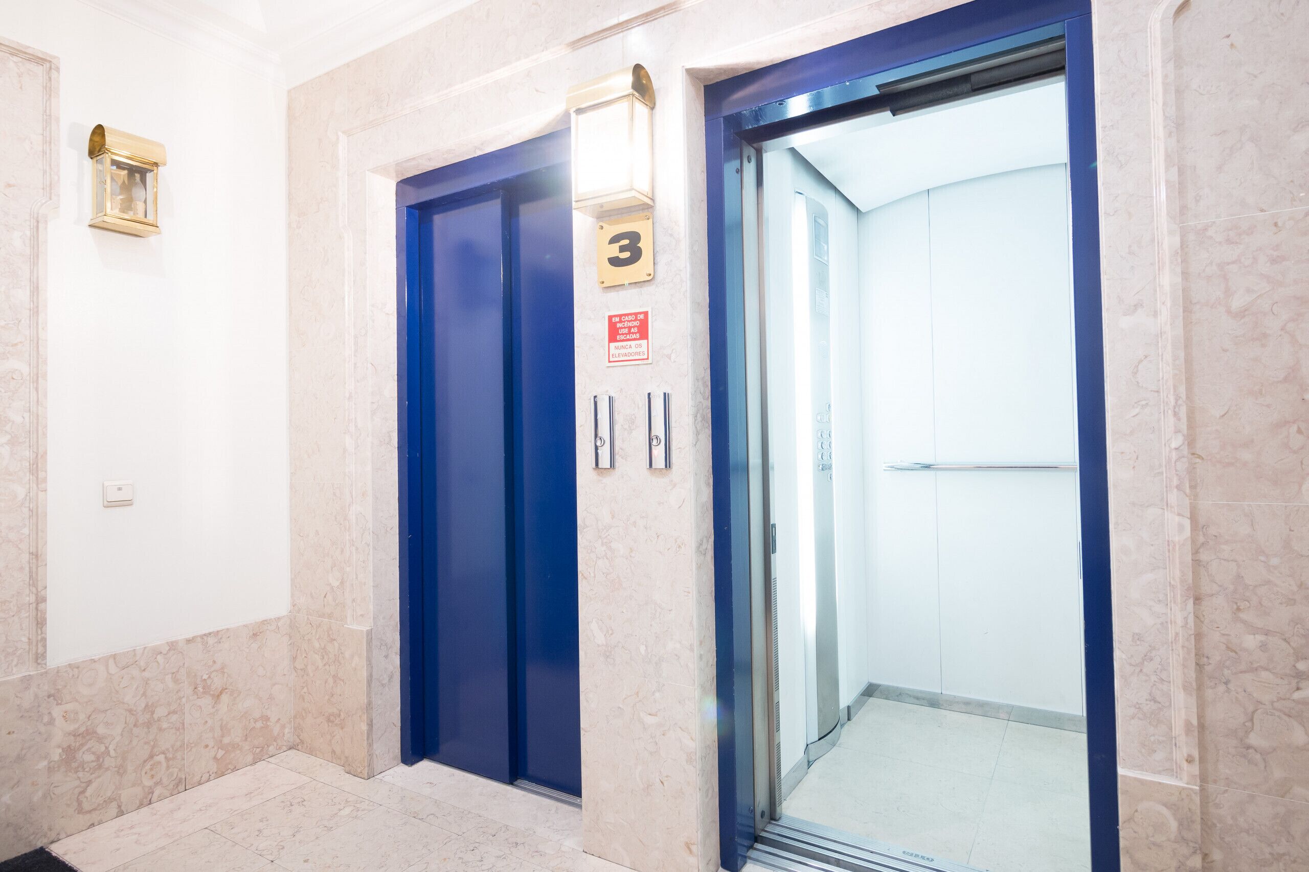 Ein Hotelfahrstuhl mit blauer Tür, einem Schild mit der Nummer 3 und einem roten Sicherheitsschild.