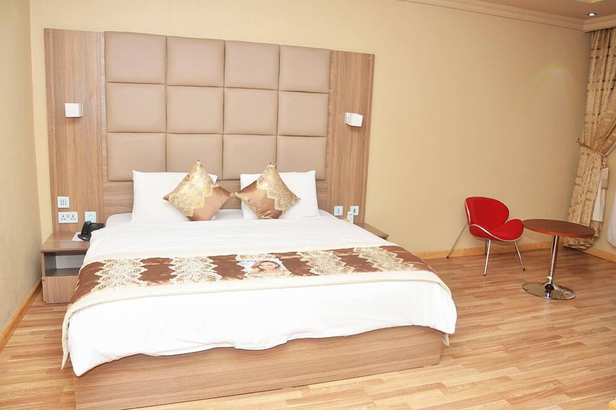A hotel room with a large bed, a wooden headboard, a small red chair, and a round table.