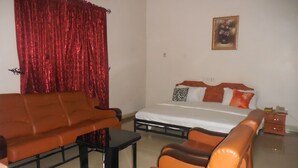 A room with a bed, a sofa, a coffee table, and a red curtain. - Amba Hotels Limited (Yenagoa)