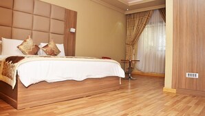 A spacious bedroom with a large bed, a wooden headboard, and a wooden floor. - Amba Hotels Limited (Yenagoa)