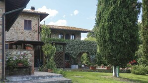 A stone building with a tiled roof, a stone pathway leading to a wooden door, and a well-maintained garden with potted plants and a tall tree. - Cosy apartment in villa for 4 guests with WIFI, pool, terrace and pets allowed (Terricciola)