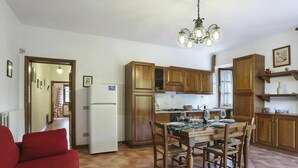 A compact kitchen with wooden cabinets, a dining table set for four, and a red sofa in the living area. - Beautiful apartment in villa for 7 people with pool, WIFI, TV, terrace and pets allowed (La Casetta)