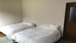 Two single beds with white bedding in a room with a wooden door and a green carpet.