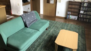 A room with a green sofa, a small wooden table, a bookshelf, and a door leading to another room.