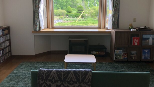 A room with a large window, a bookshelf, a small table, and a green couch.