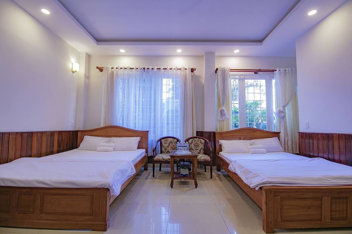 A hotel room with two wooden beds, a small table, and a chair.