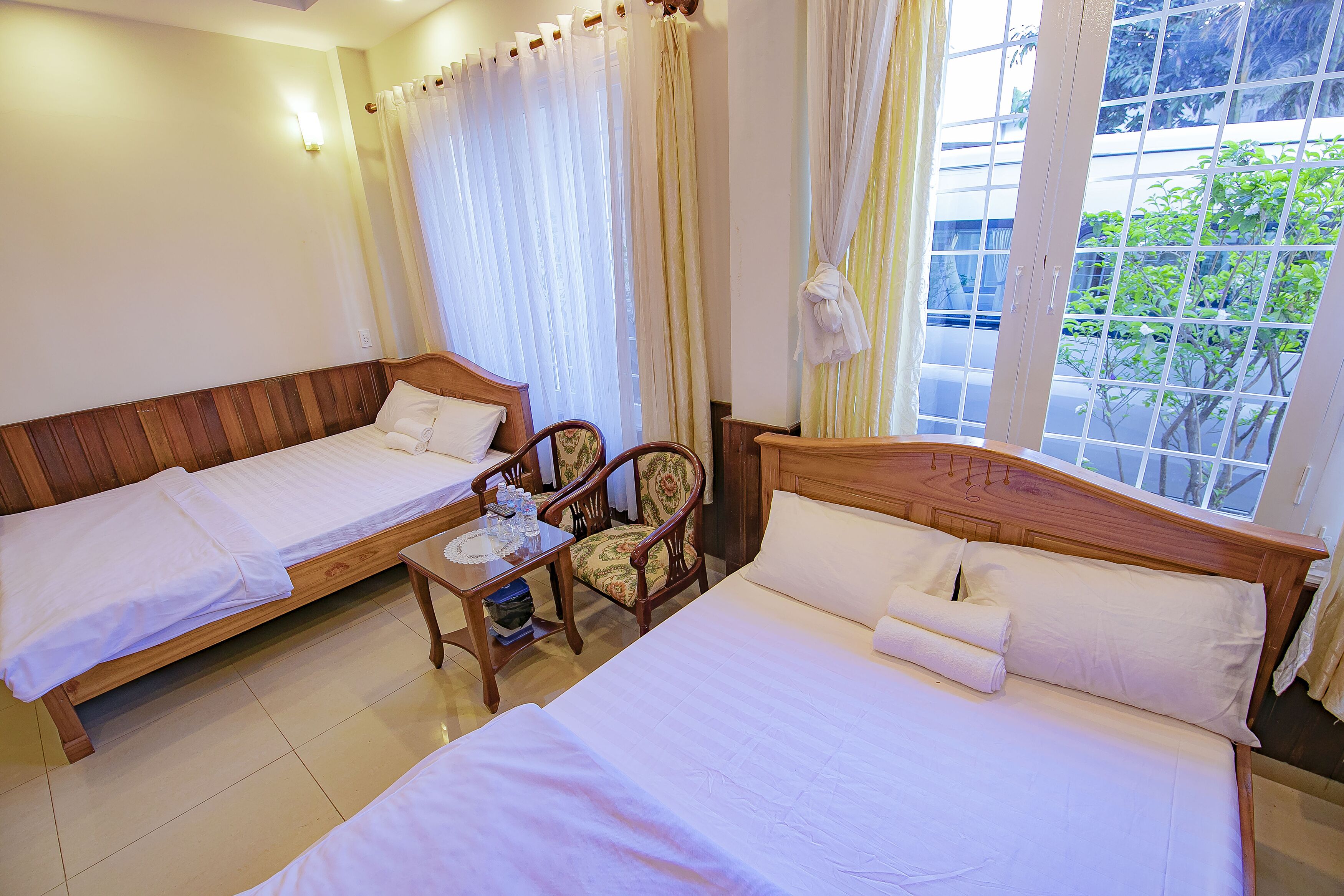 Habitación de hotel con dos camas individuales, un cabecero de madera, una mesita con una silla y una ventana con cortinas.