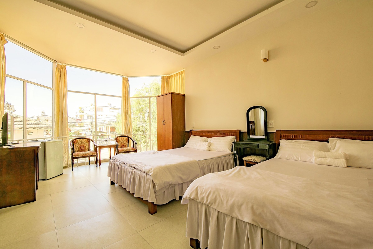 Une chambre d’hôtel avec deux lits, un bureau, une chaise et une grande fenêtre.