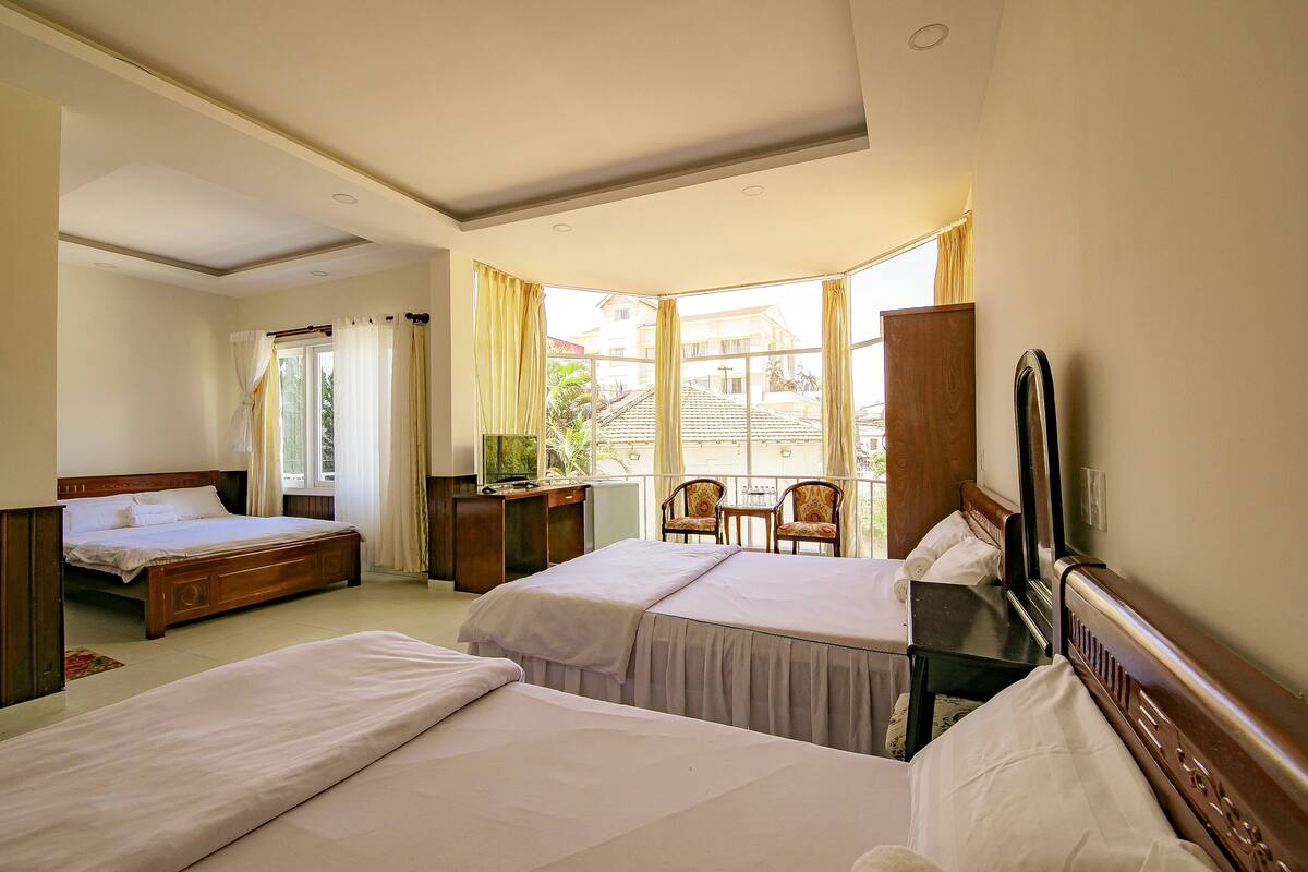 A hotel room with two beds, a desk, a chair, and a large window with curtains.