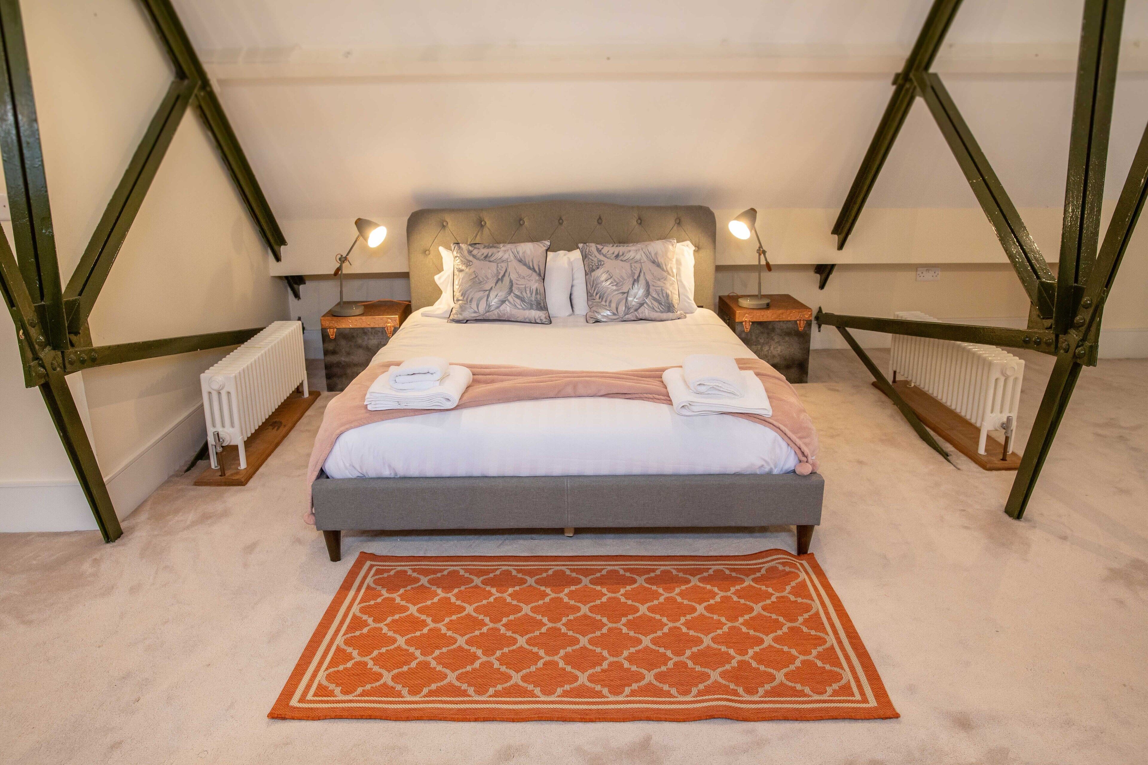 Une chambre à coucher avec un lit, deux tables de chevet, un radiateur et un tapis à motifs.