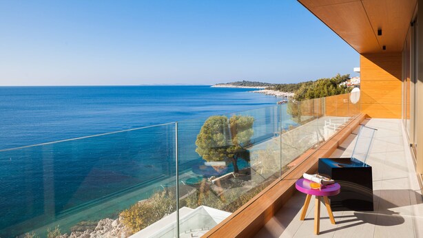 Un balcón con vistas despejadas al mar, suelo de madera y barandilla de cristal.