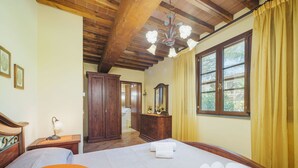 Un dormitorio con una cama grande, un armario de madera, un escritorio con lámpara y una ventana con cortinas.