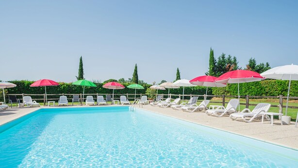 Una piscina con sillas de descanso blancas y sombrillas.