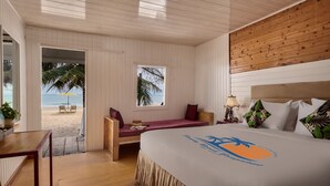 A hotel room with a wooden ceiling, a bed with a tropical-themed bedspread, a desk, a window with a view of the beach, and a small seating area with a table and chairs. - Sandy Beach Bungalows by EHM (Koh Rong Sanloem)