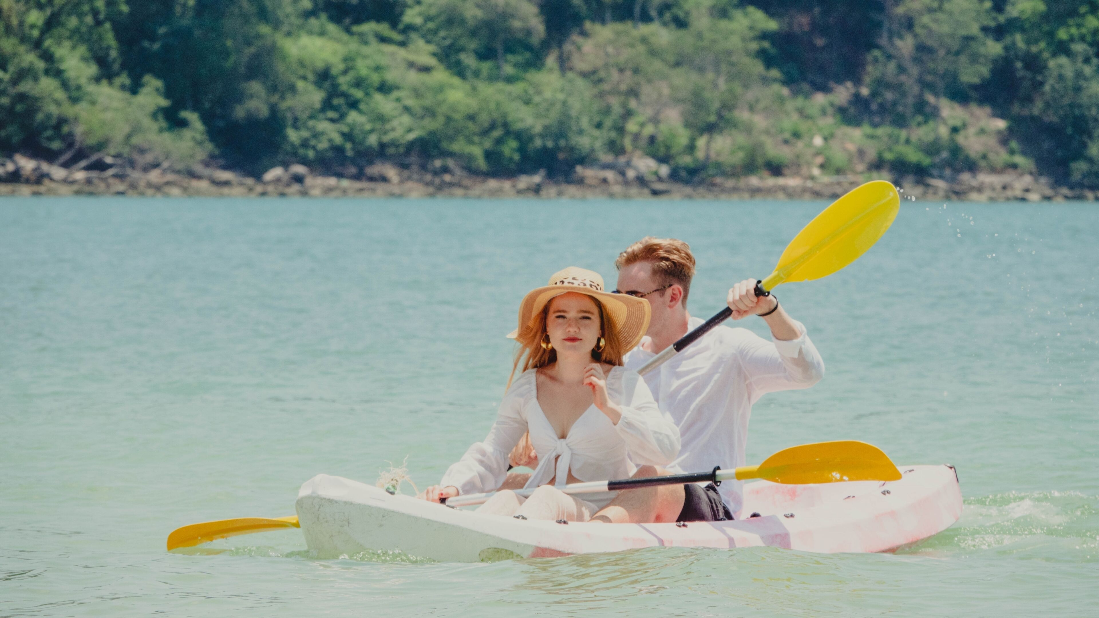 A couple in a kayak on a calm body of water with a forested shoreline in the background.