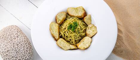 Une assiette blanche contenant des spaghettis et du pain, posée sur une surface blanche.