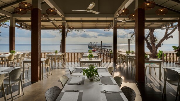 A seaside restaurant with tables and chairs, a ceiling fan, and a view of the ocean. - Sandy Beach Bungalows by EHM (Koh Rong Sanloem)