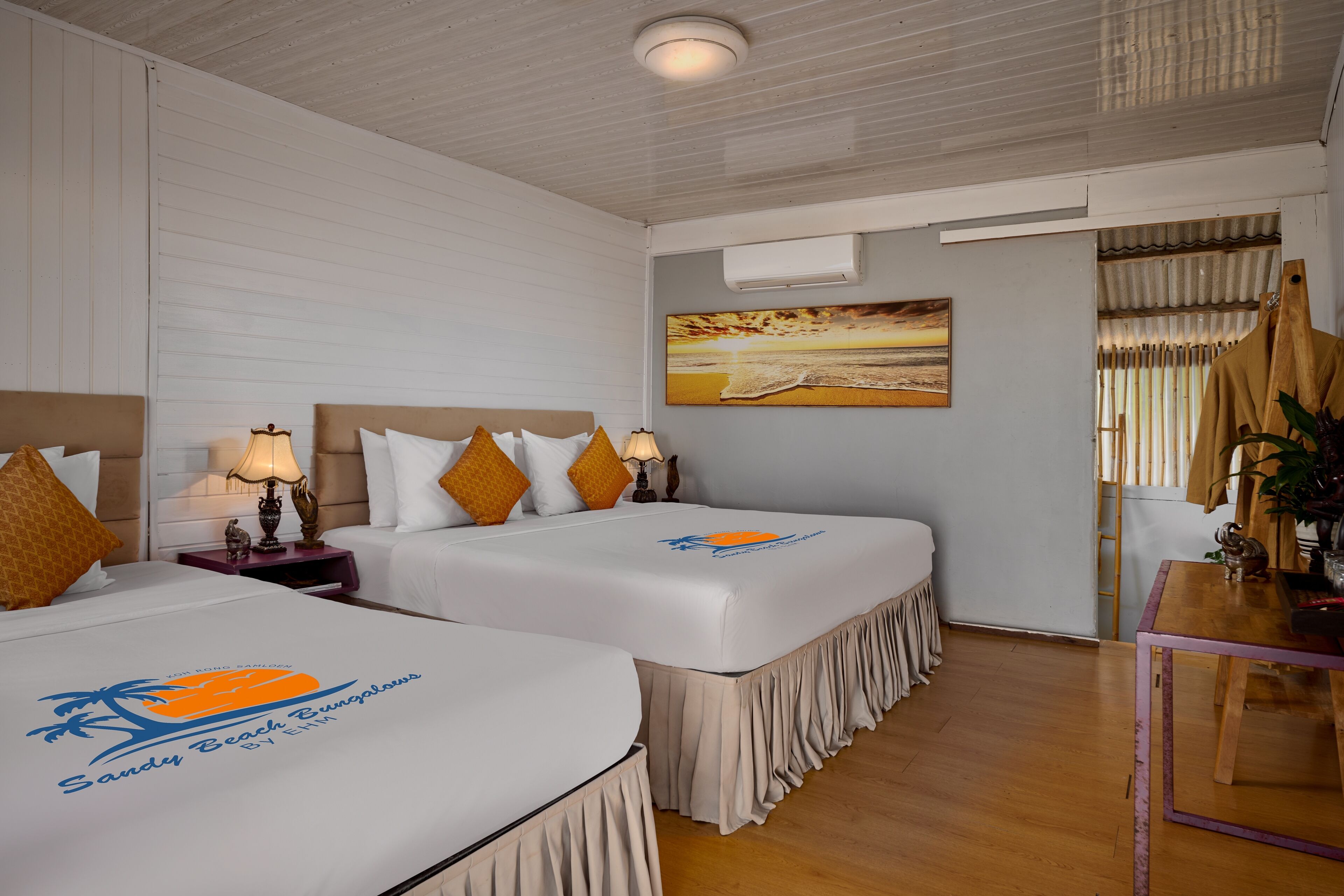 Een hotelkamer met twee bedden, een schilderij, een houten tafel en uitzicht op het strand.